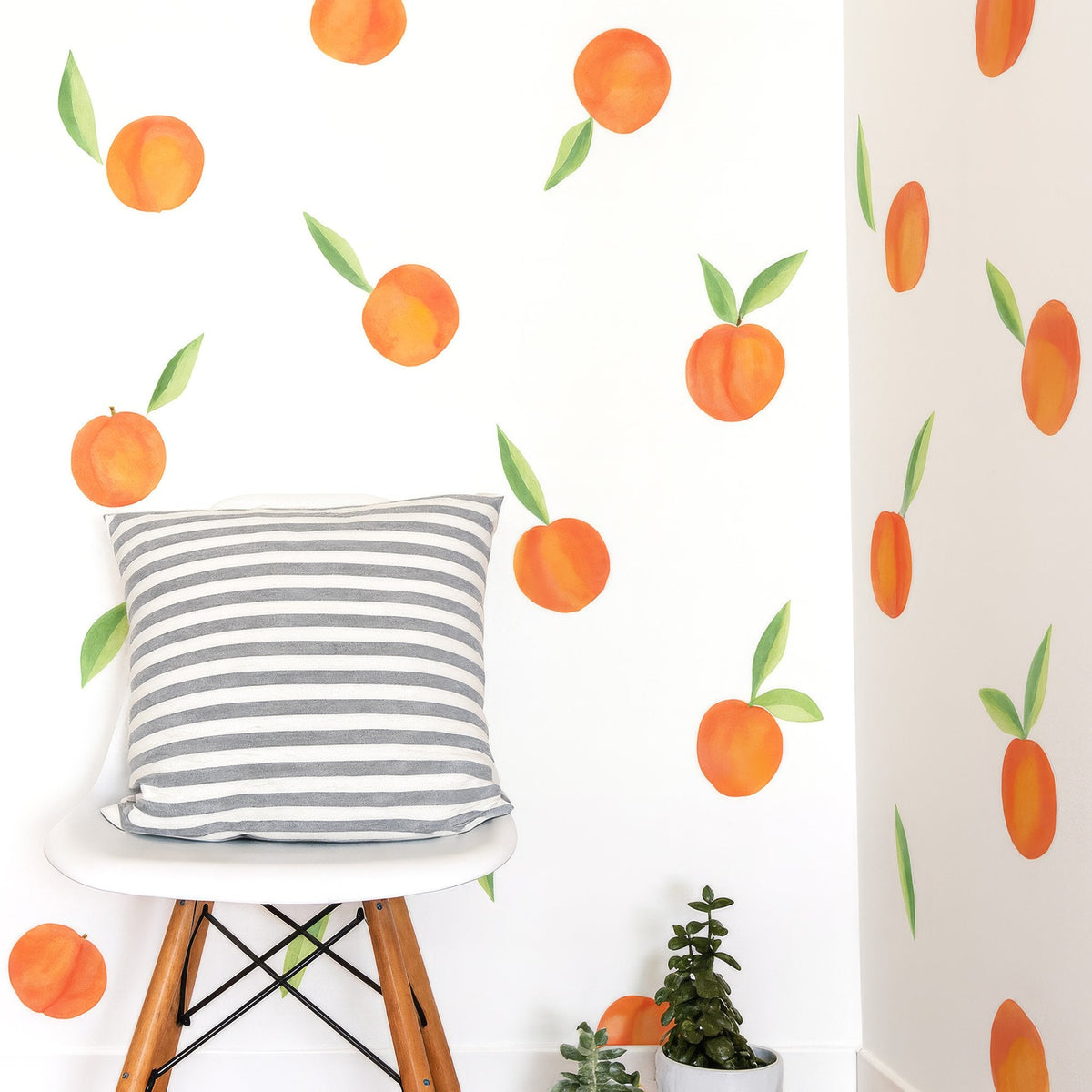 Watercolor peach wall decals styled on a white corner wall with a striped pillow on a modern chair and small succulents