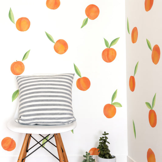 Watercolor peach wall decals styled on a white corner wall with a striped pillow on a modern chair and small succulents